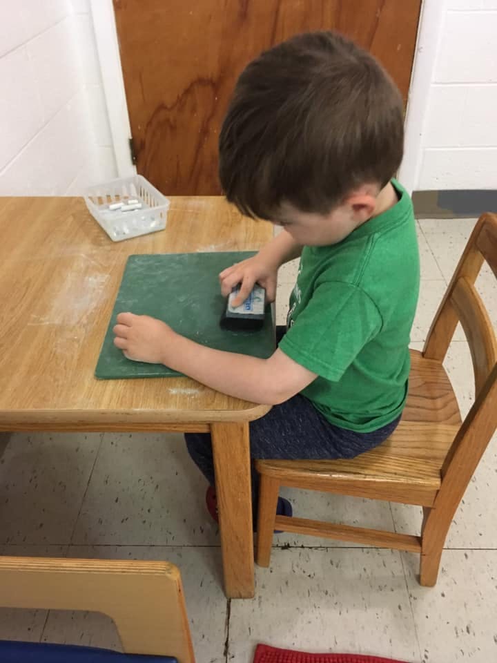 Child sitting at a table using a small tool on a green mat