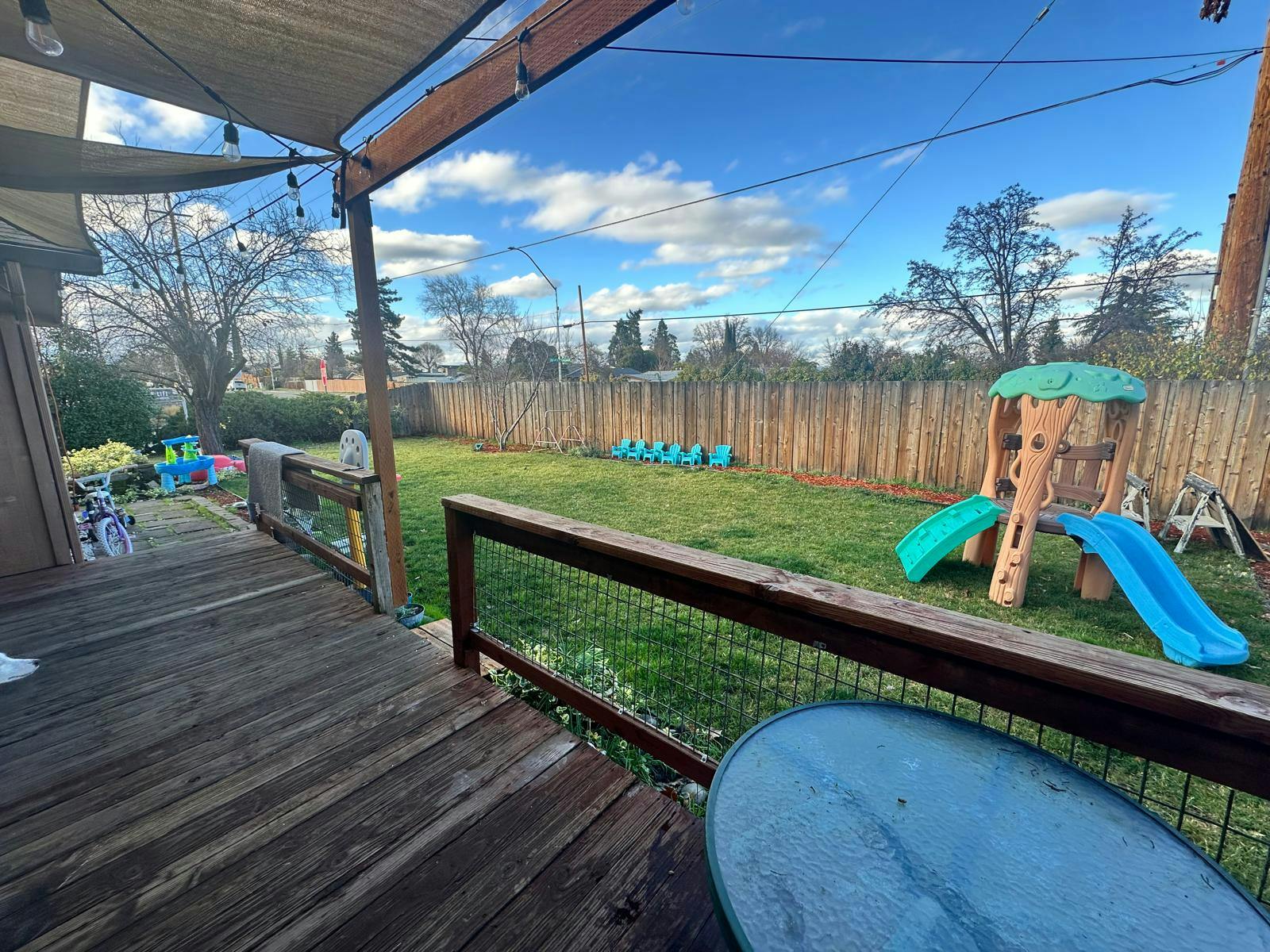 Backyard with a wooden deck, green lawn, and a small play structure with slides
