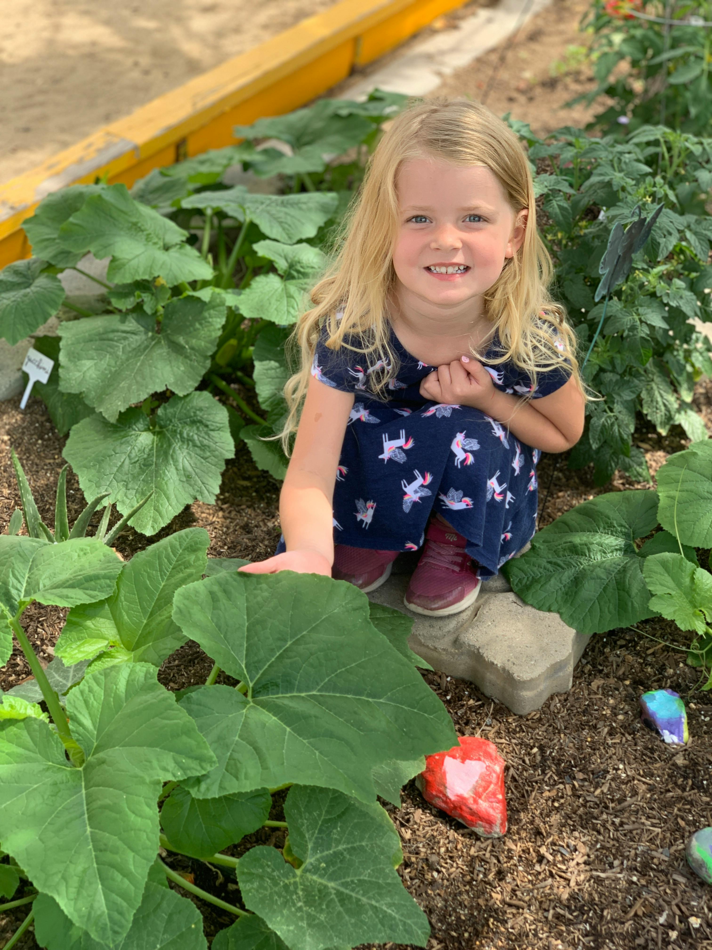 Child kneeling in a garden with large green leaves