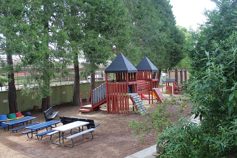 Playground with wooden play structure, slides, and picnic tables under trees