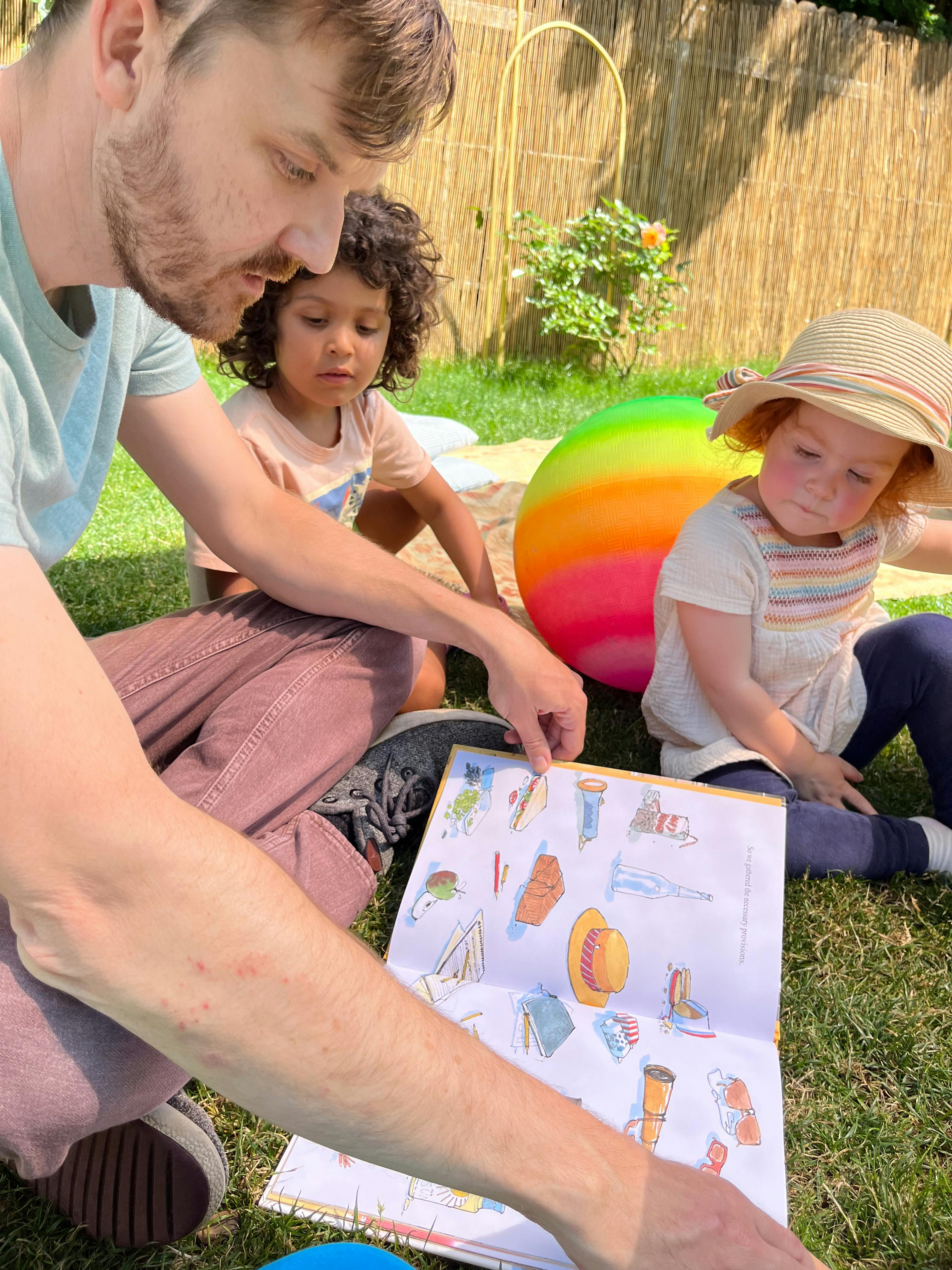 Person and two children looking at a book outdoors
