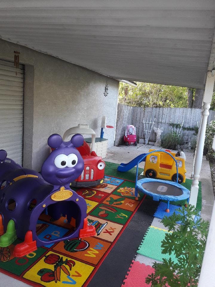 Outdoor play area with a purple caterpillar tunnel, red car, yellow bus slide, and trampoline