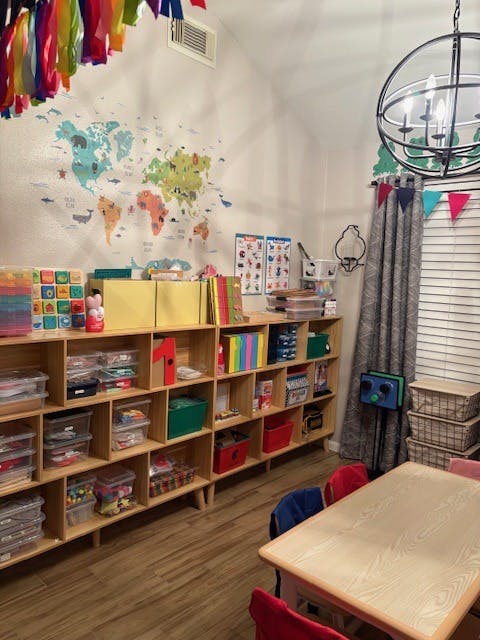 Classroom with world map mural, shelves full of supplies, and small table with chairs