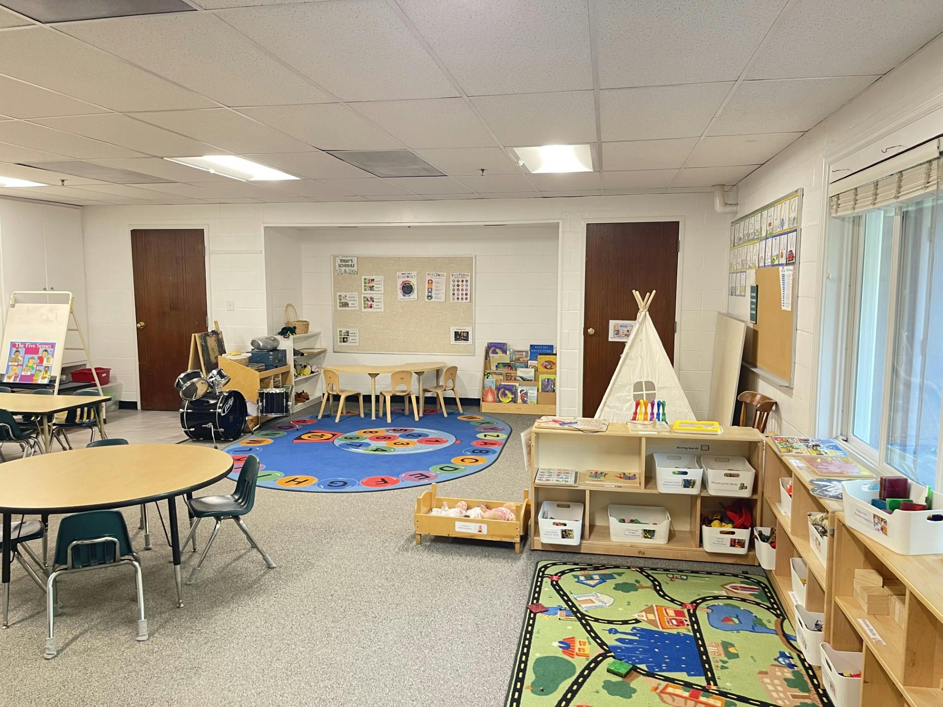 Classroom interior with tables, a play tent, and educational rugs