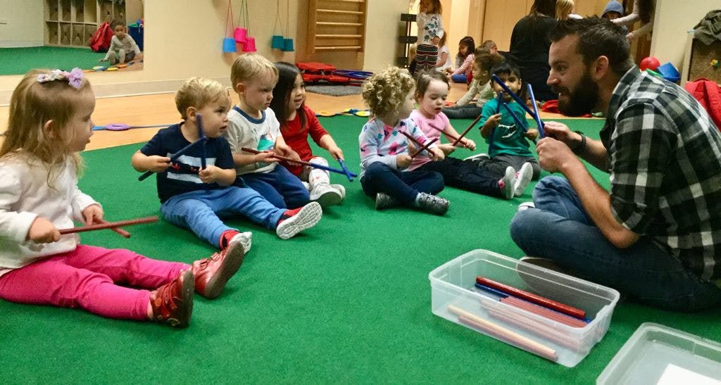 Adult and children sitting on floor holding sticks