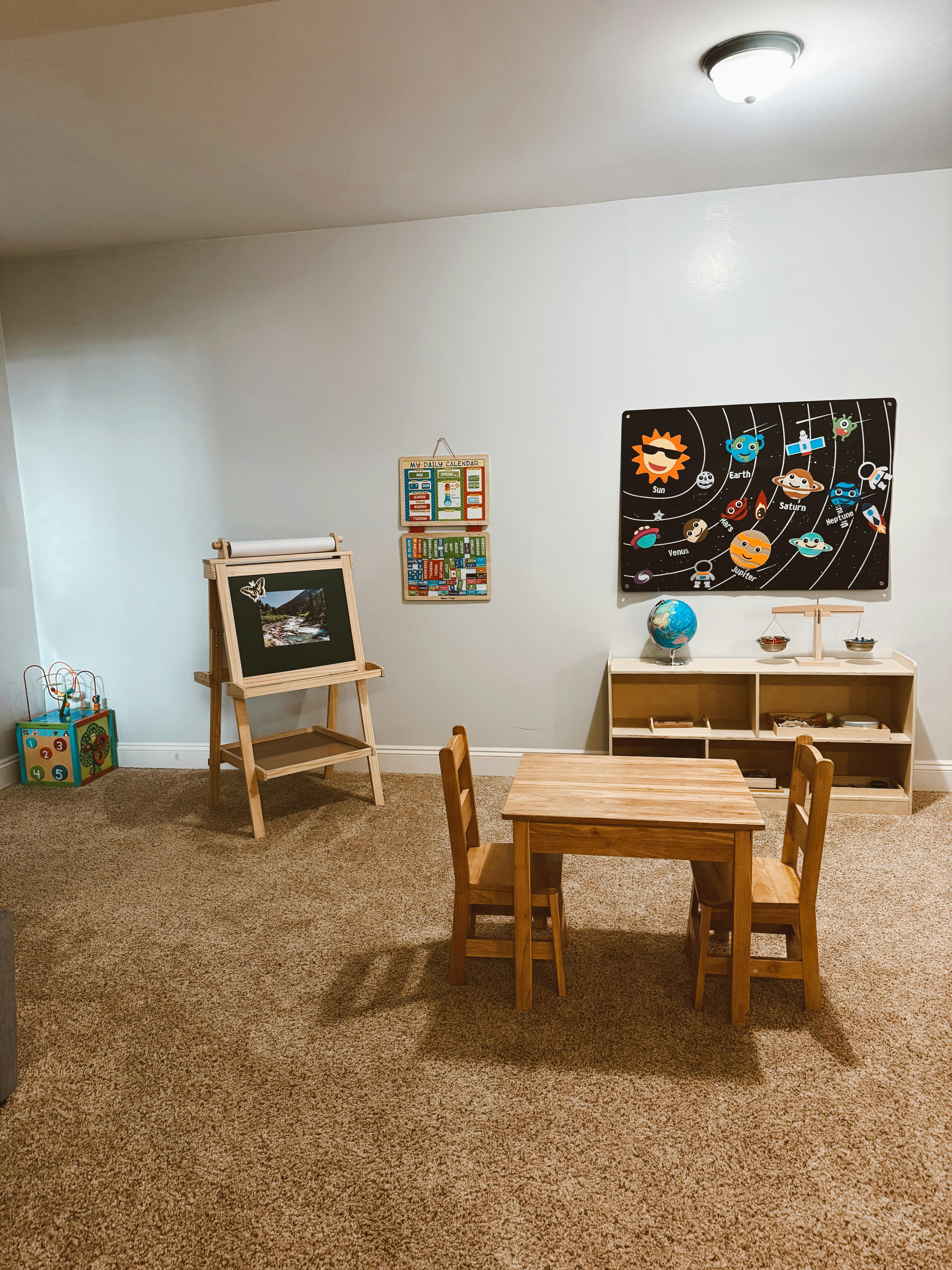 Children's play area with a small table and chairs, easel, and solar system poster