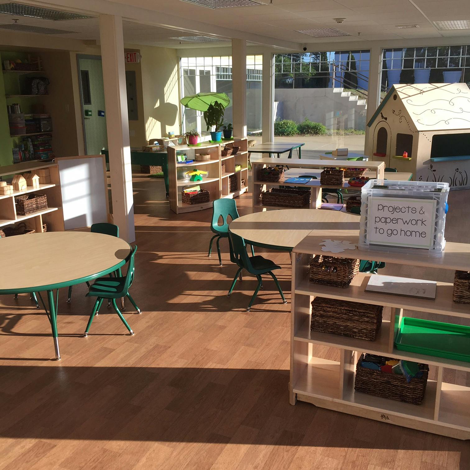 Classroom with small tables and chairs, shelves with baskets, and a playhouse