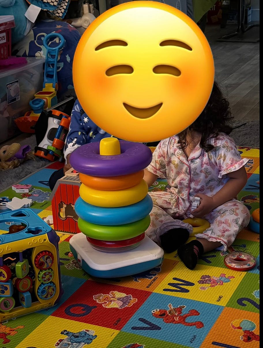 Child sitting on a playmat next to a colorful stacking ring toy