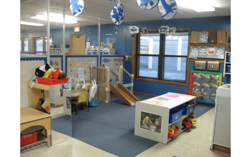 An indoor classroom or play area with a small slide, tables, and toys