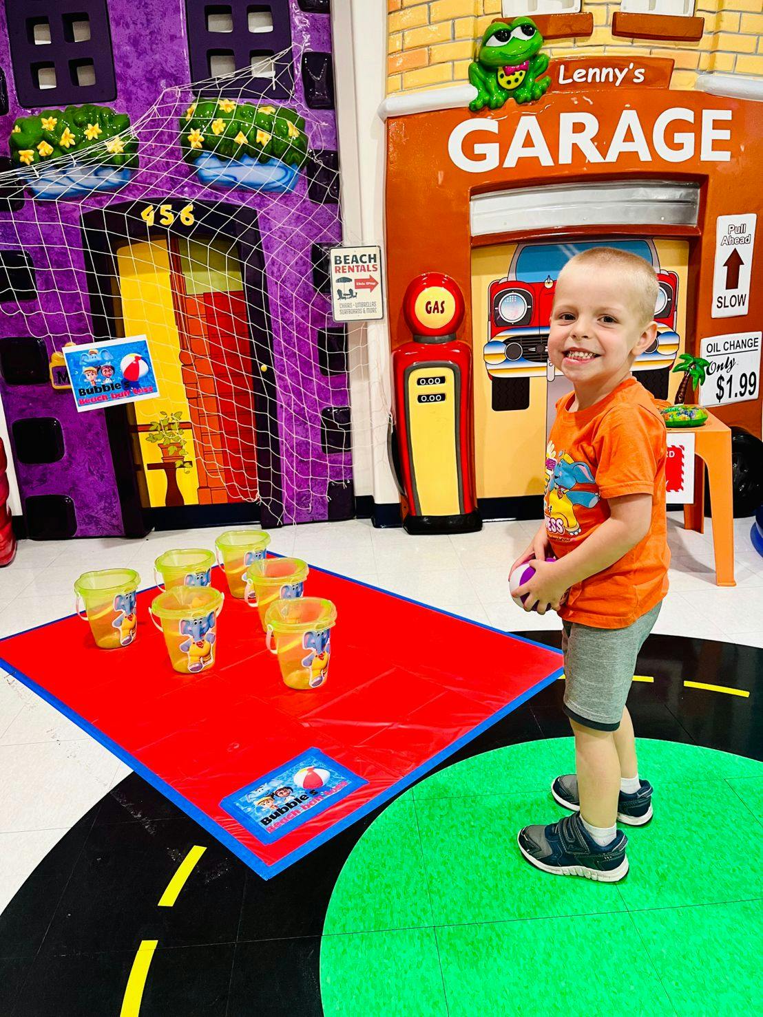 Child holding a ball, standing next to a game with buckets