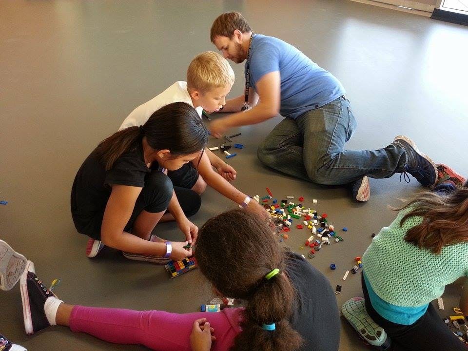 Adult and children on floor playing with small building blocks