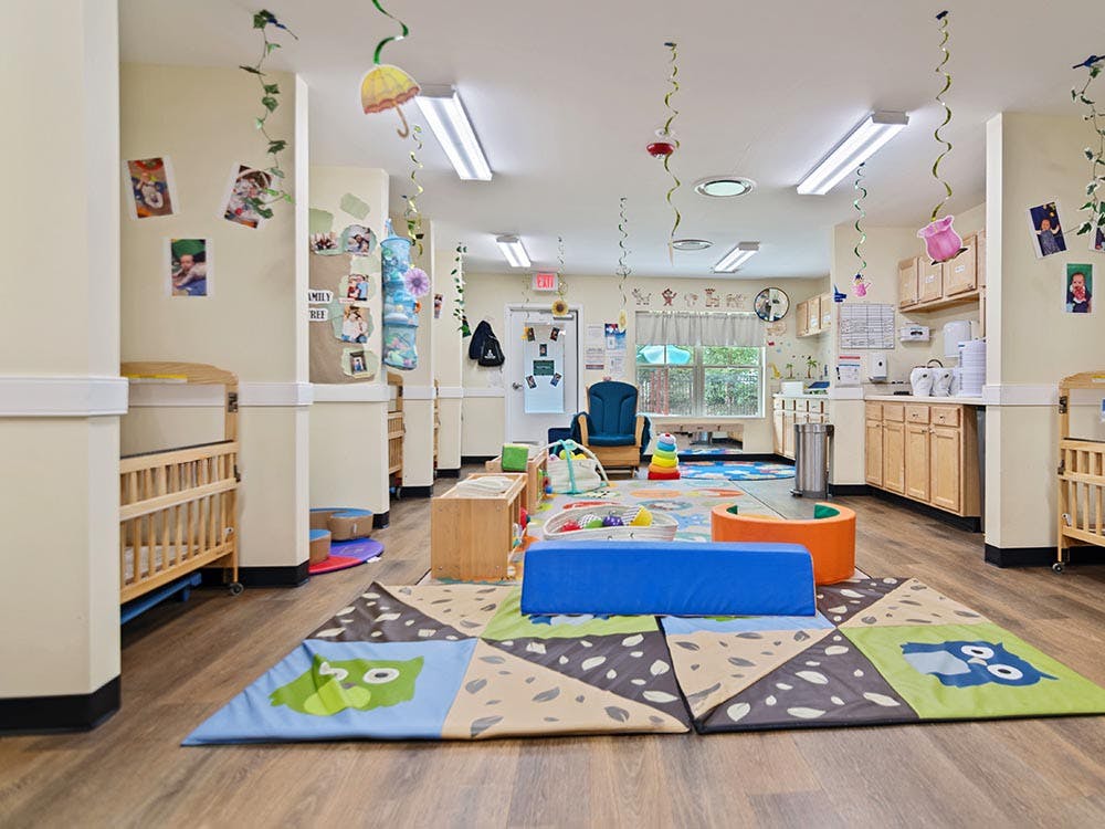 A colorful childcare classroom with cribs, playmats, and cabinets