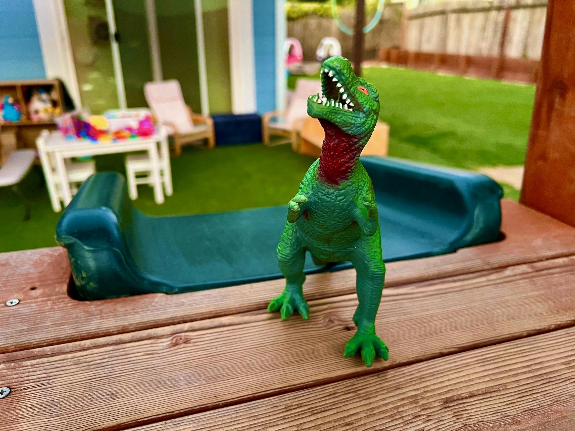 Green toy dinosaur with an open mouth on a wooden surface