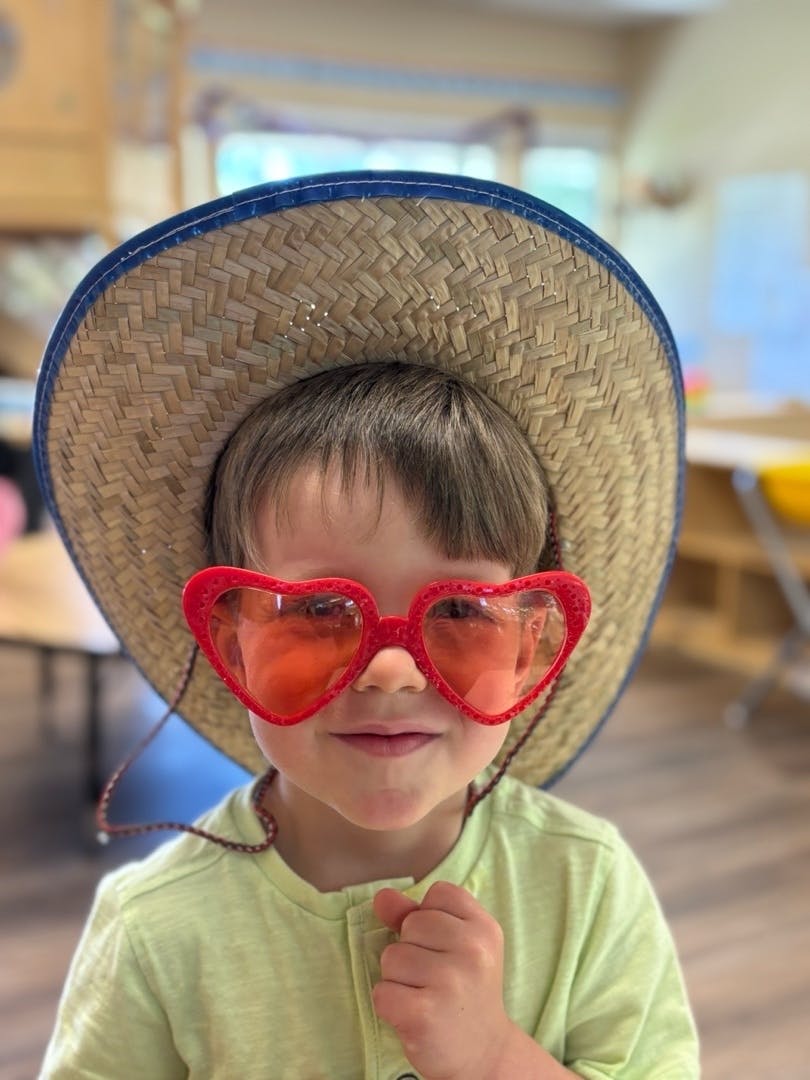 Child wearing a straw hat and red heart-shaped sunglasses