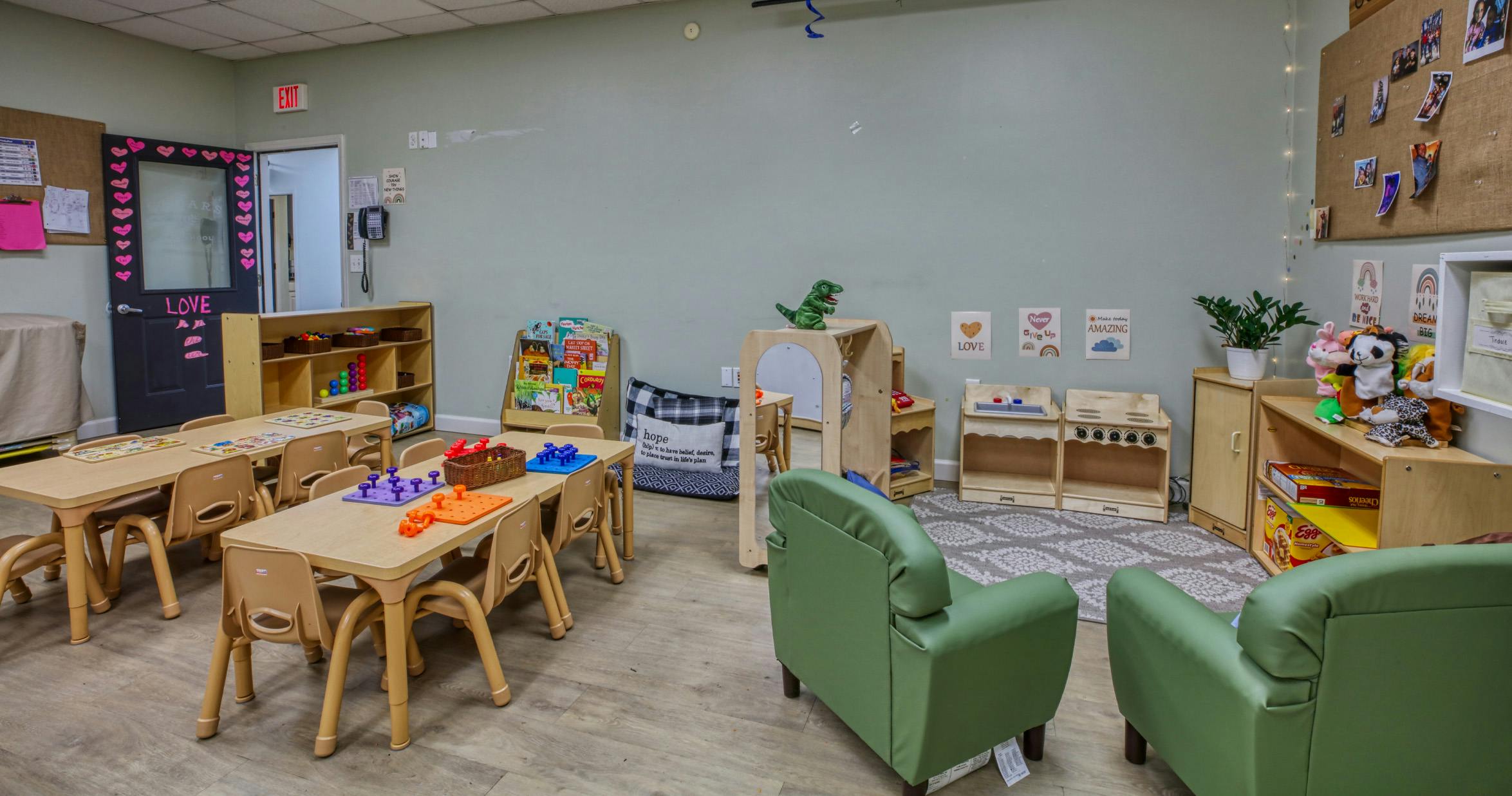 Children's classroom with small tables and chairs, toys, and green armchairs