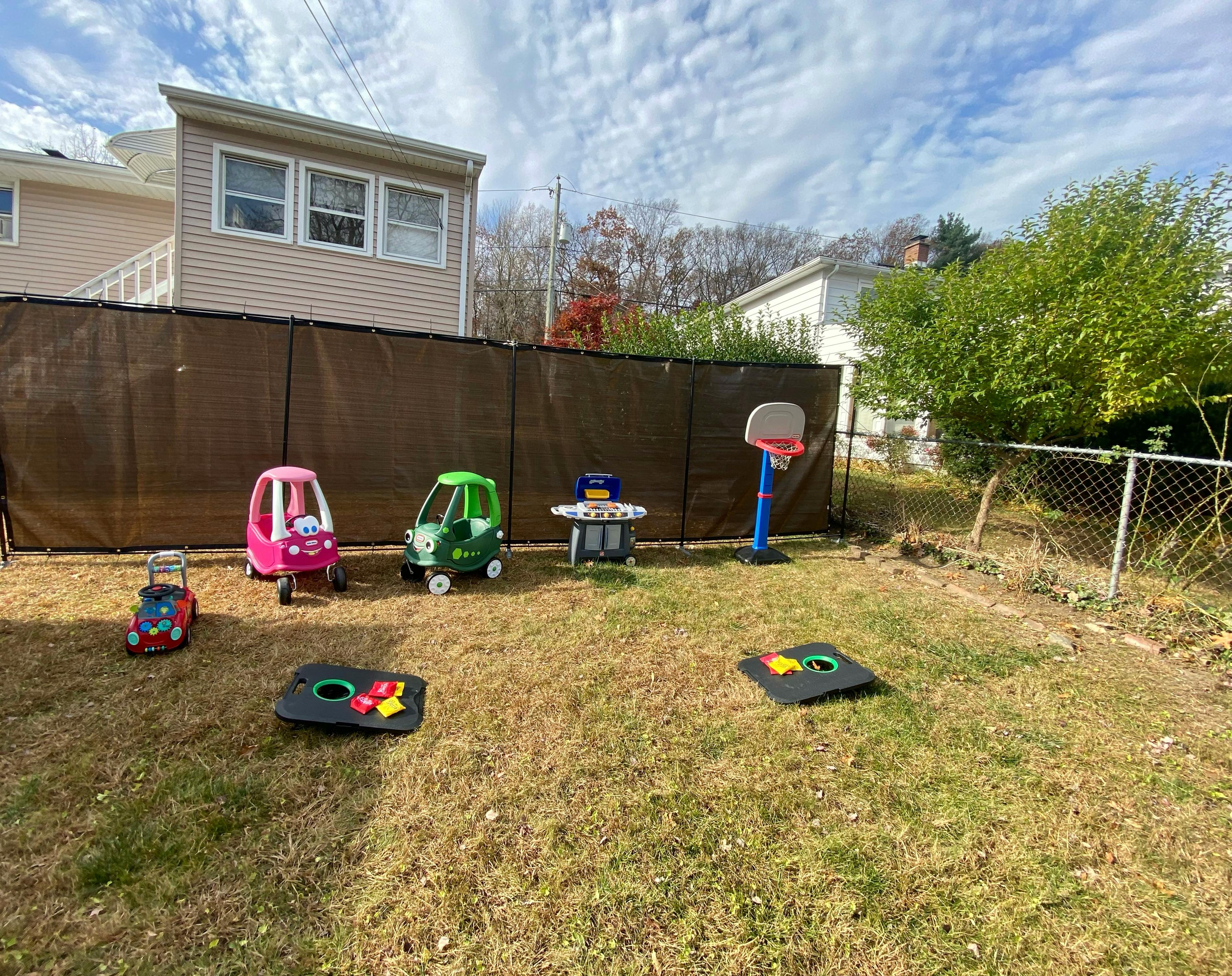 Toy cars, a basketball hoop, and cornhole boards in a grassy yard