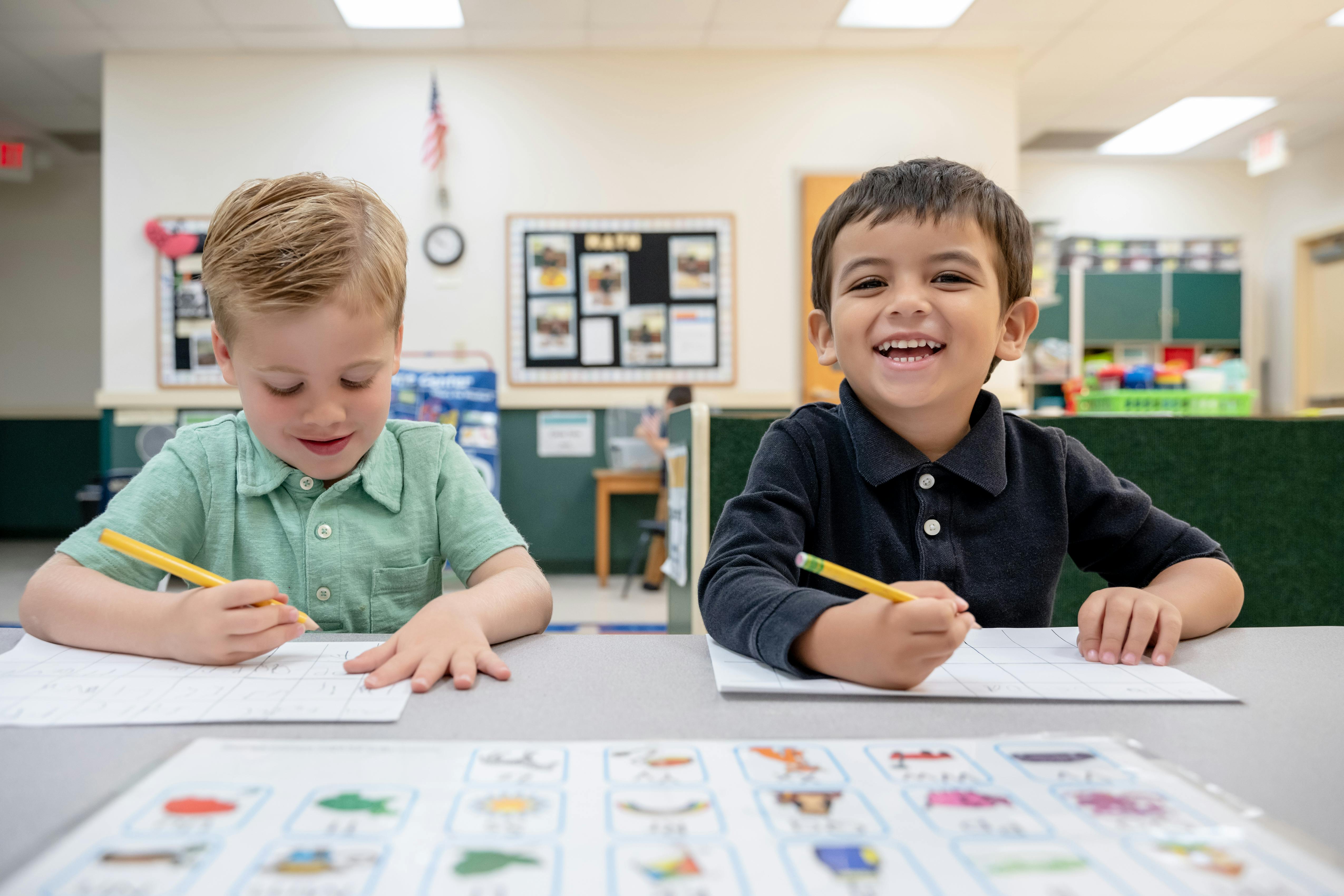 Two children writing at a table in a classroom
