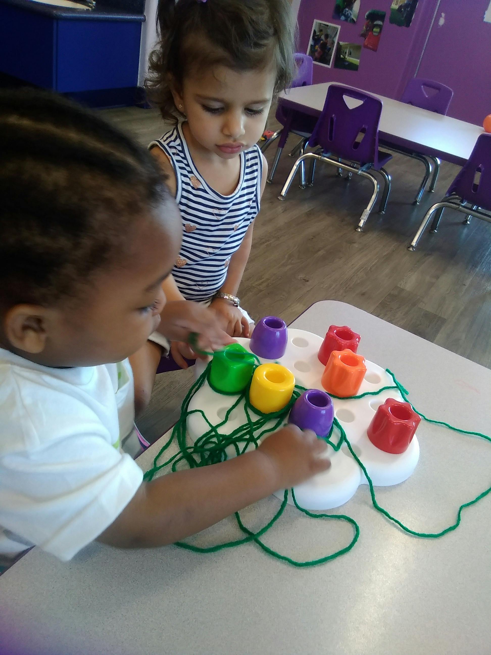 Two children playing with a lacing toy