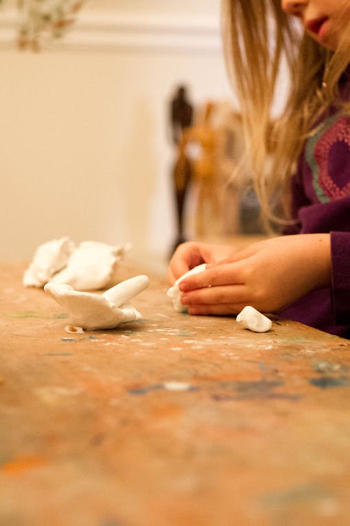 Child's hands molding white clay on a wooden table