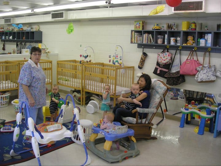 Two people and multiple children in a room with cribs and baby equipment
