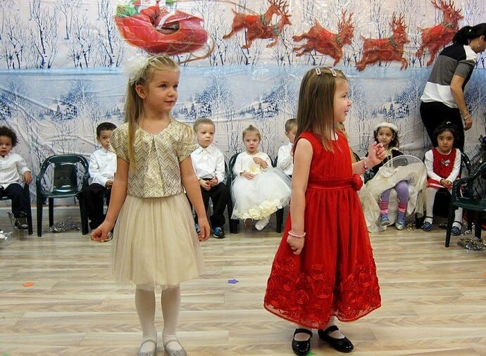 Two children in dresses standing in front of other children seated