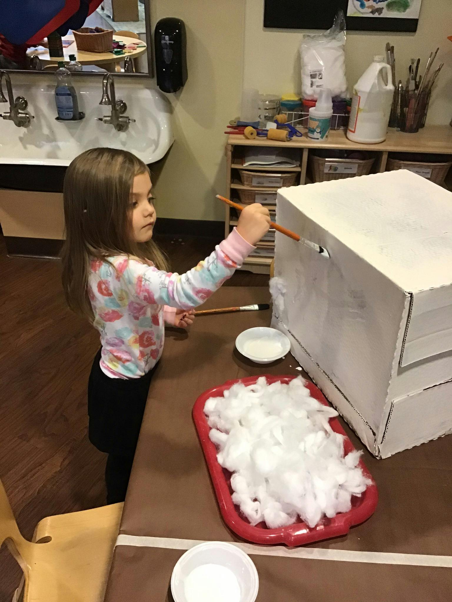 Child painting a white box with a paintbrush
