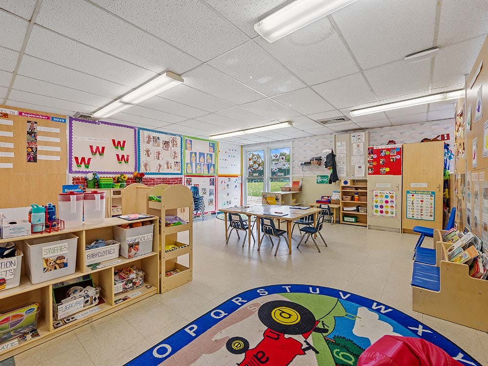 An empty early childhood classroom with tables, chairs, and shelves
