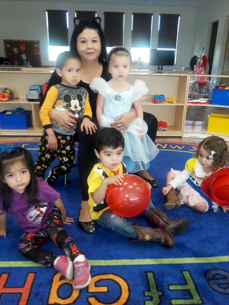 Person with cat ears holding two children, with three other children on the floor