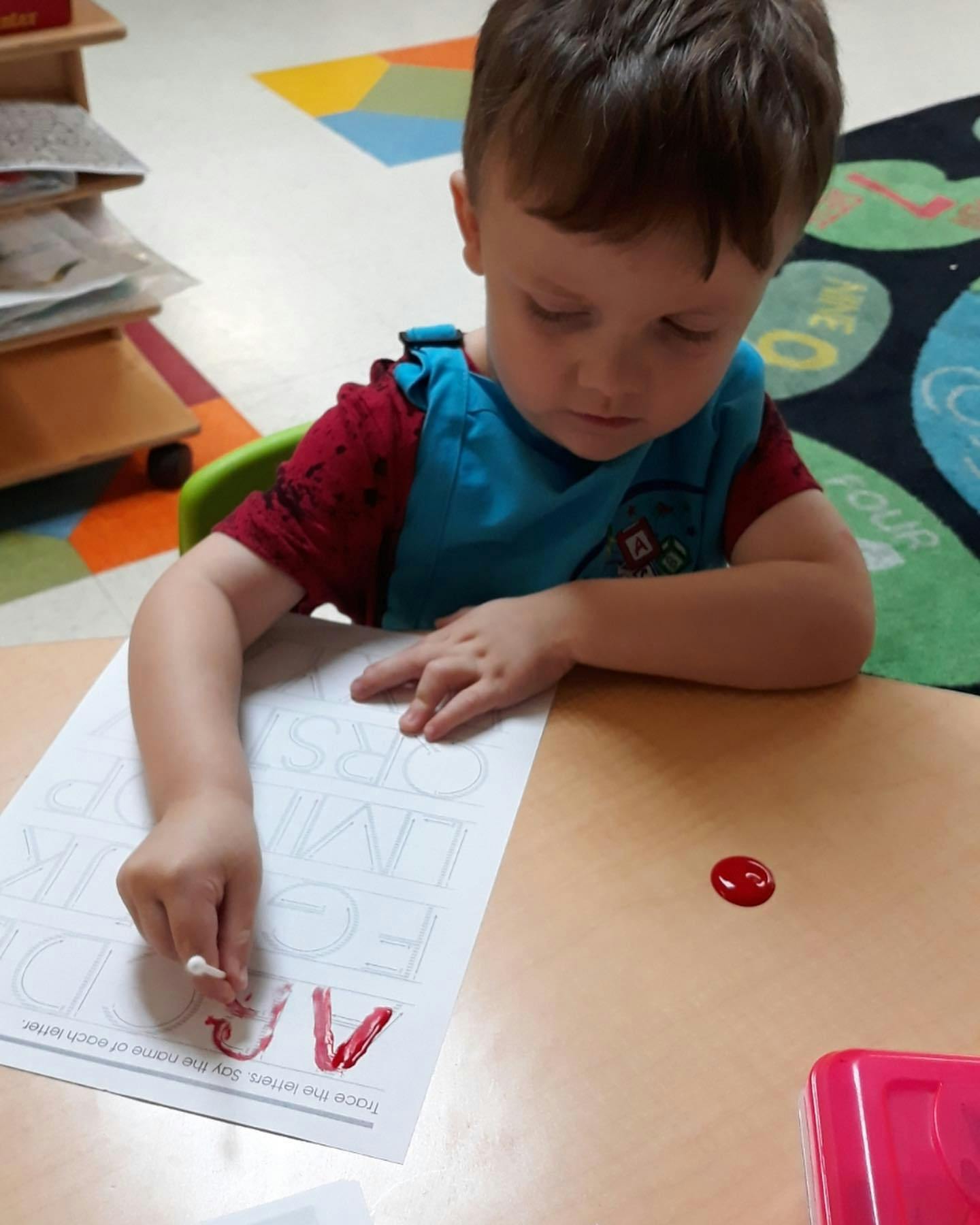 Child tracing letters on paper with a red marker