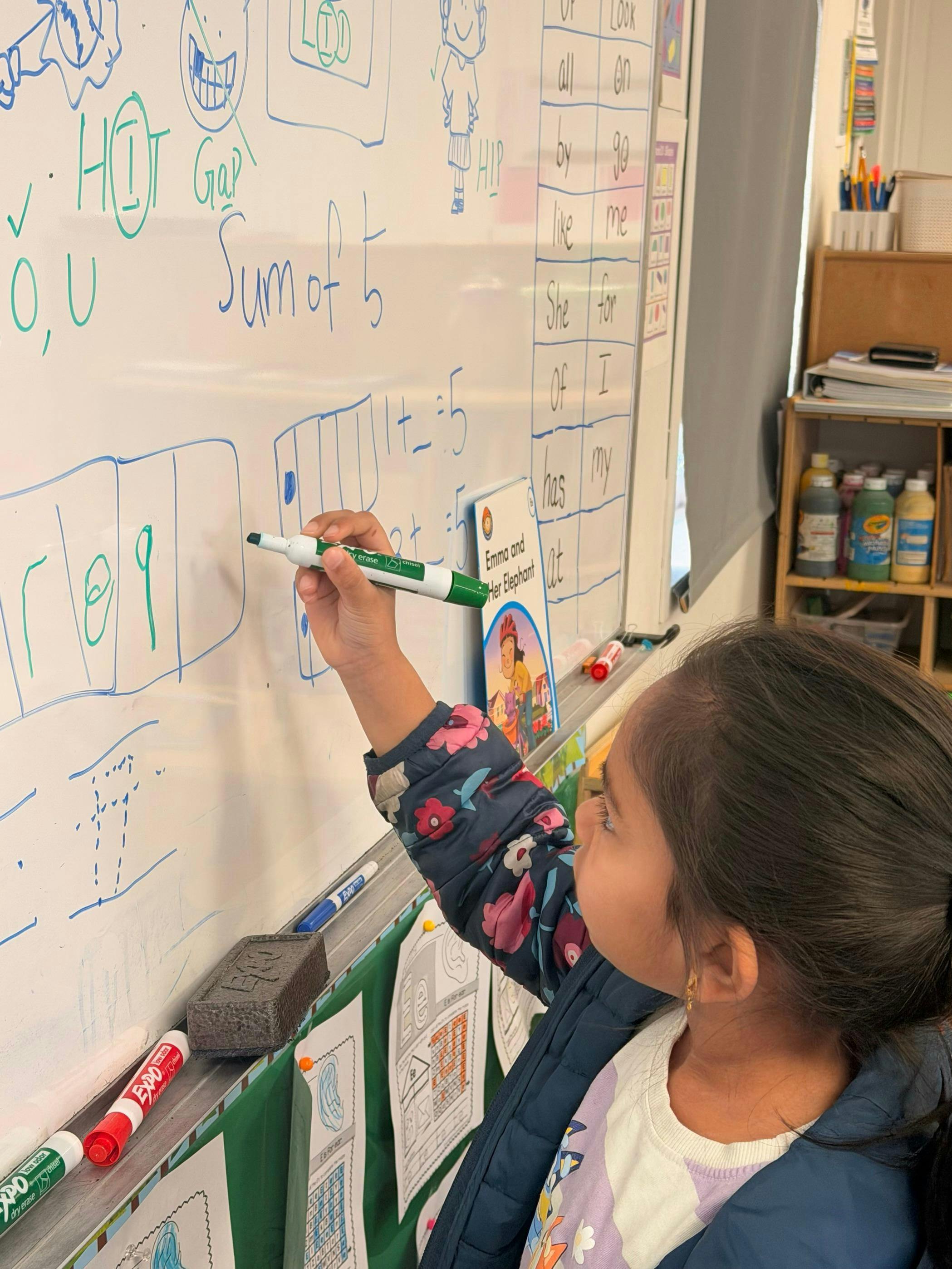 Child drawing on a whiteboard with a green marker