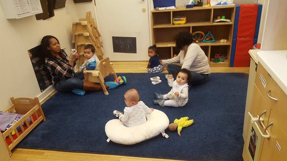 Two adults and multiple babies on a blue rug in a room