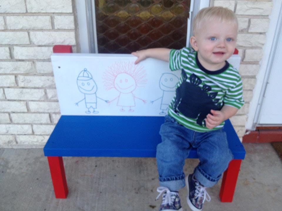 Child sitting on a small bench with drawings on the backrest