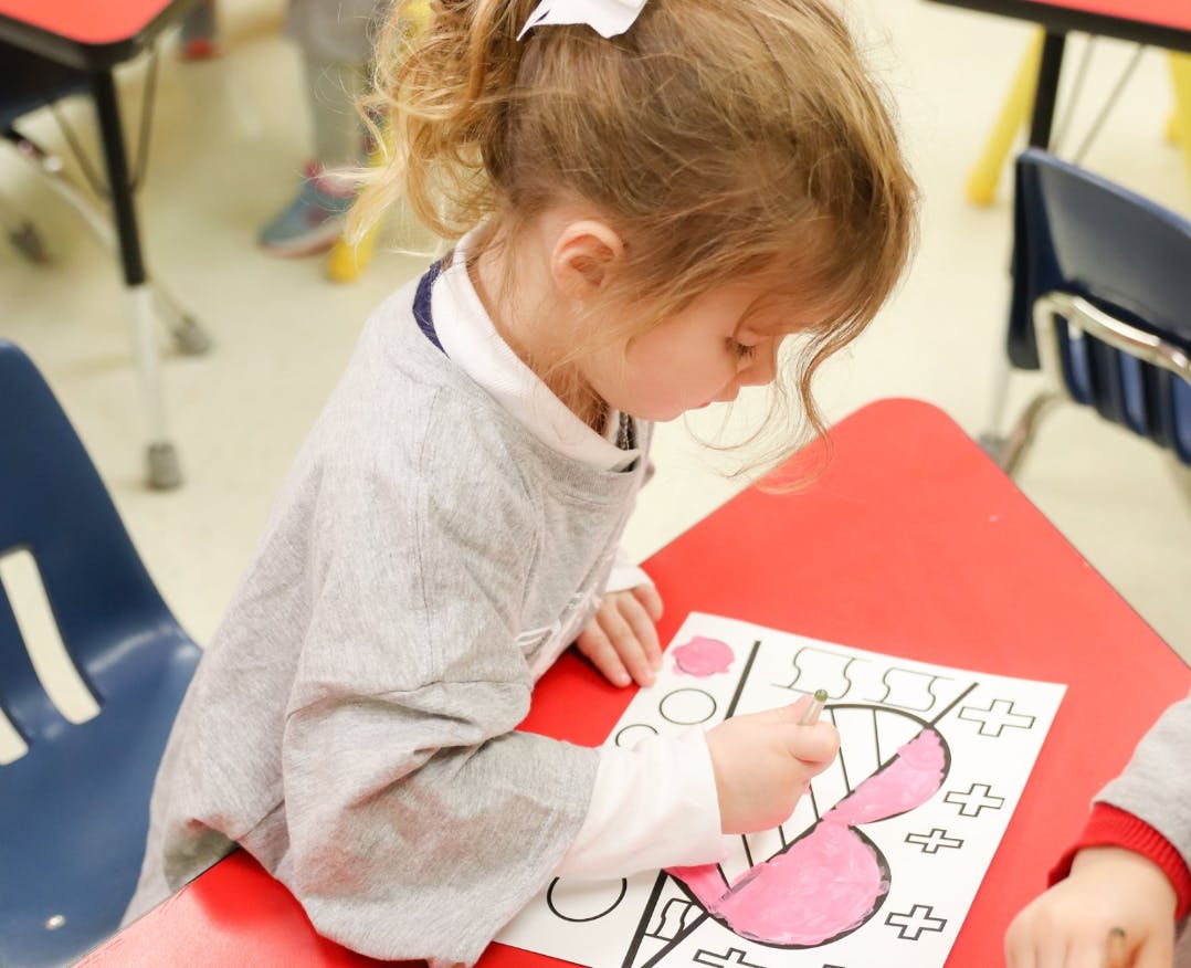 Child coloring a heart on a red desk