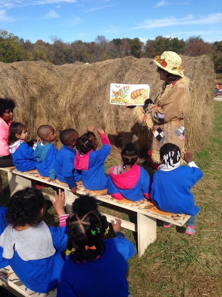 Person in straw hat reading a book to children sitting on a bench outdoors
