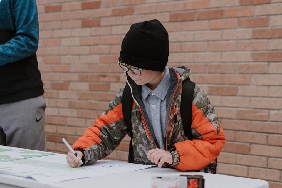 Child in beanie and jacket writing on paper atable