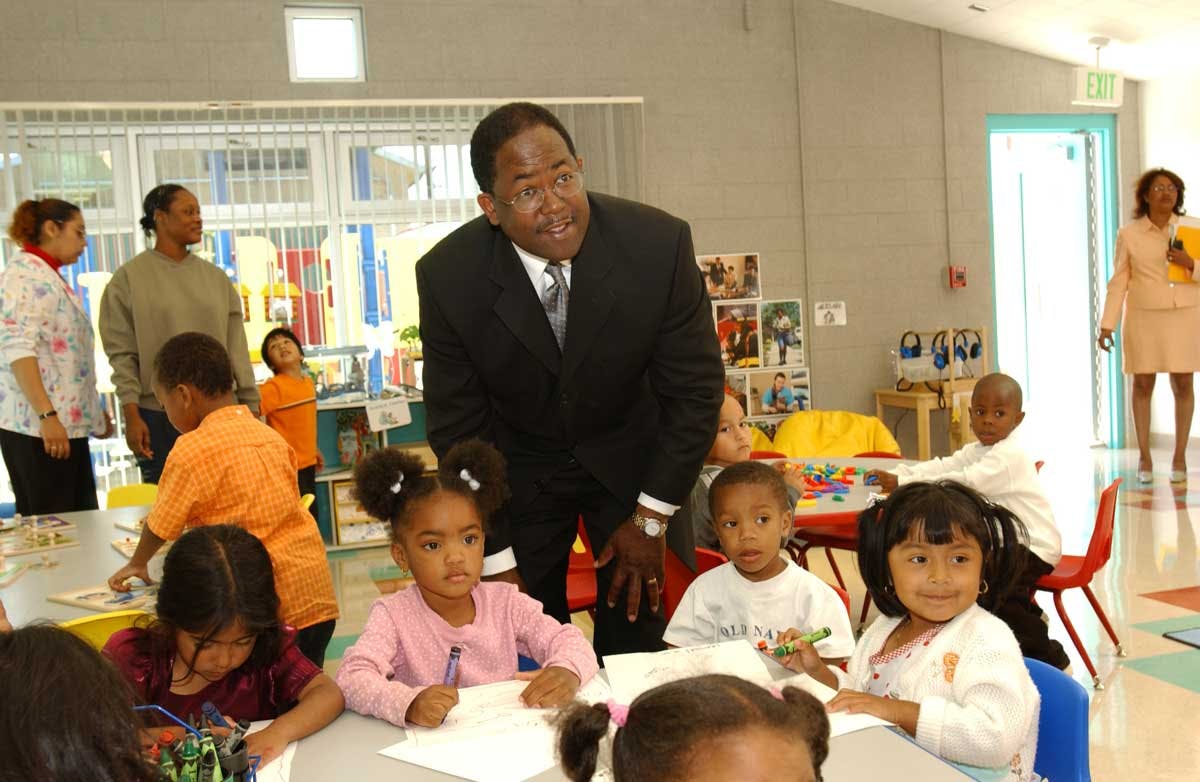 Adult person interacting with children drawing at tables in a classroom