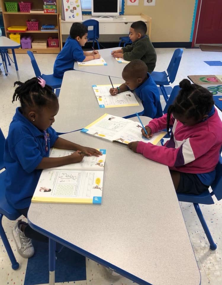Children sitting at tables and writing in books and on papers in a classroom