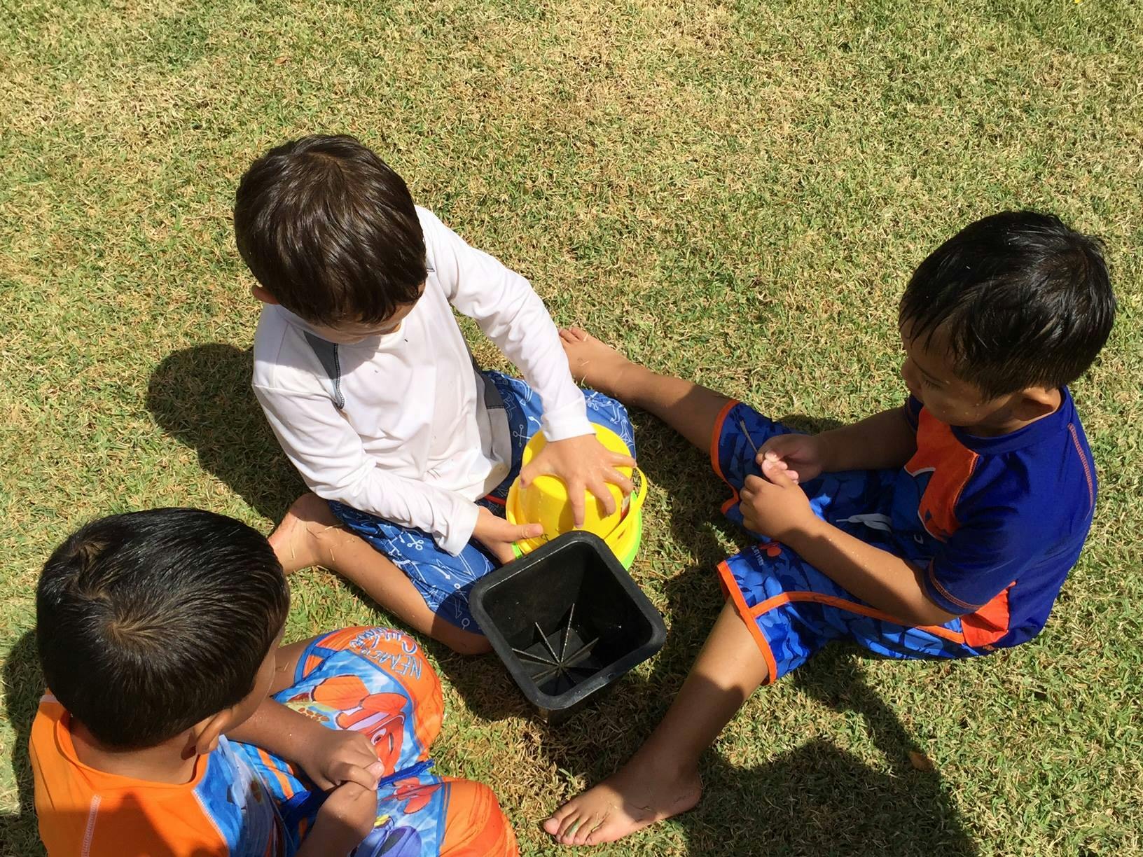 Three children sitting on grass playing with buckets