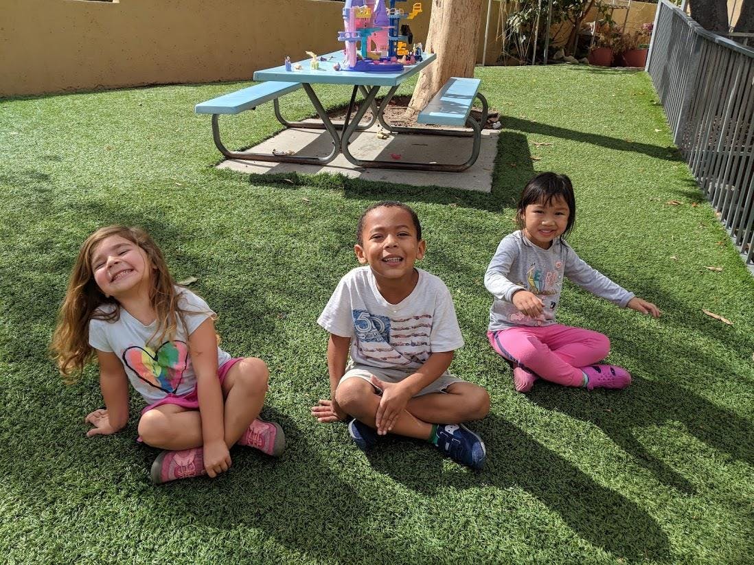 Three children sitting on artificial grass