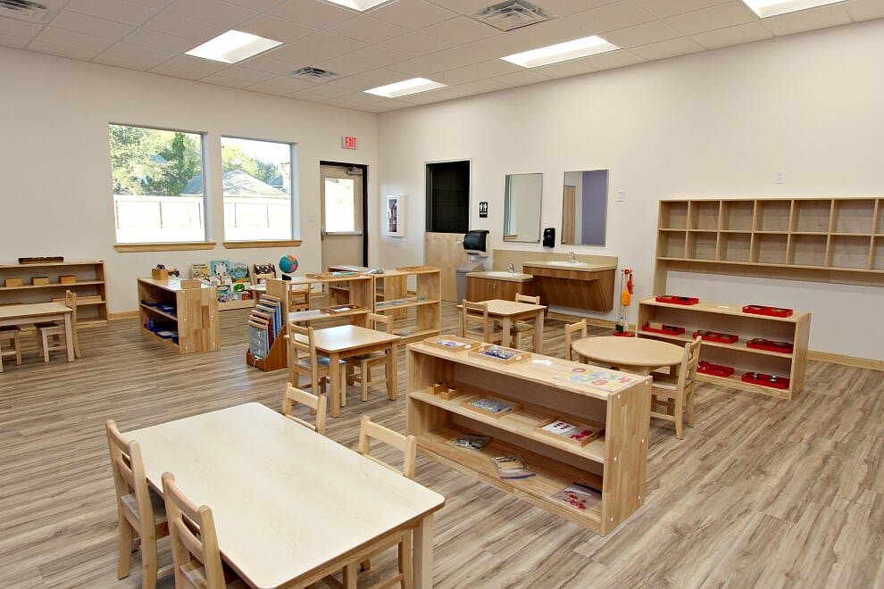 Empty classroom with small wooden tables, chairs, and shelves