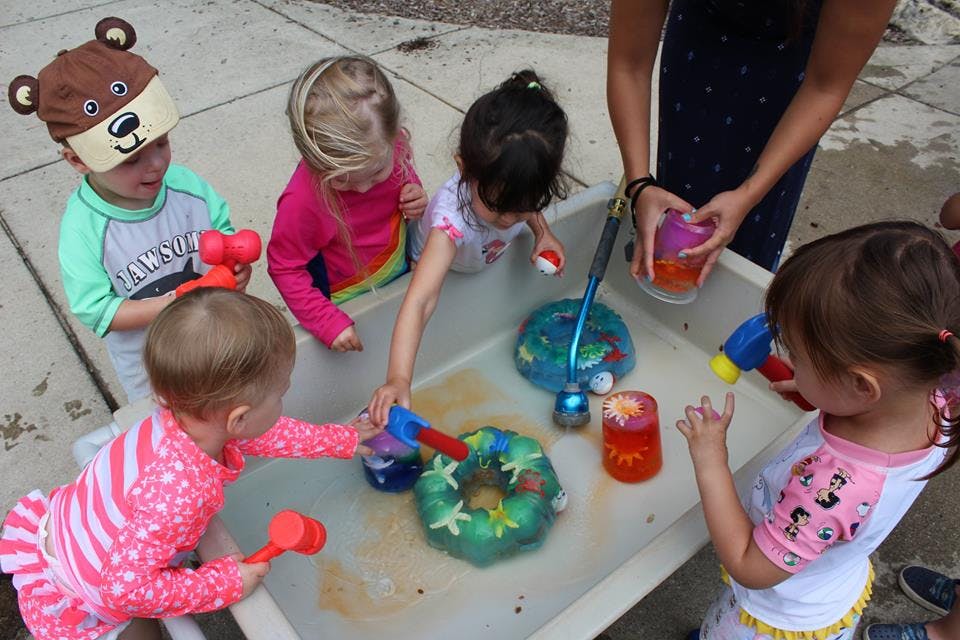 Children playing with water and toys in a sensory bin with an adult