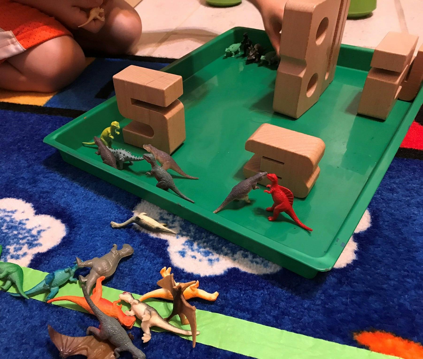 Child playing with dinosaur toys and wooden blocks on a green tray
