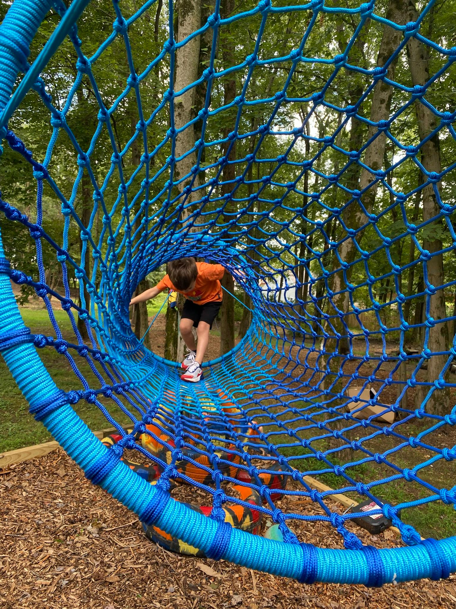 Child walking through a blue rope tunnel on a playground