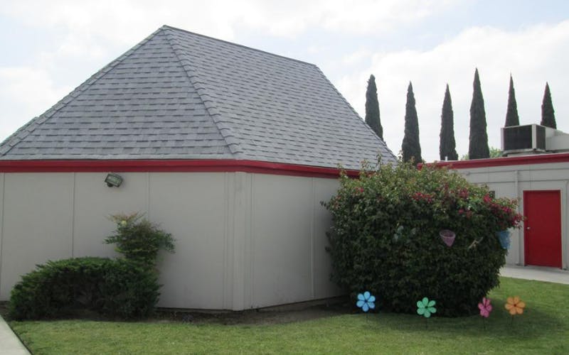A beige building with a gray shingled roof, a red trim, and red doors