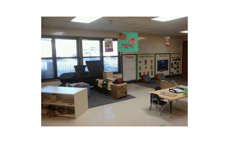 Classroom with large windows, bulletin boards, small tables, and play area