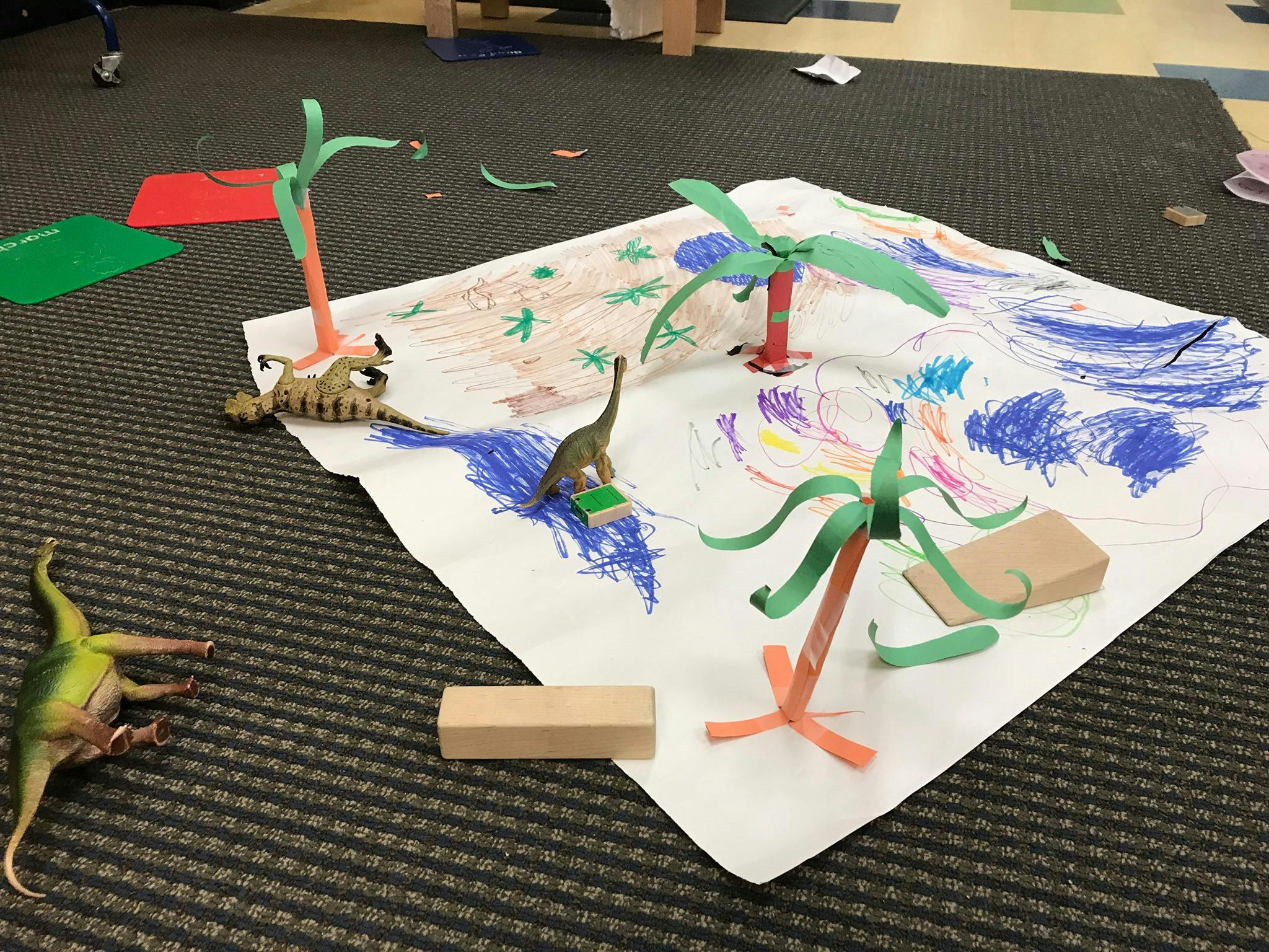 Dinosaur toys and paper palm trees on a child's drawing