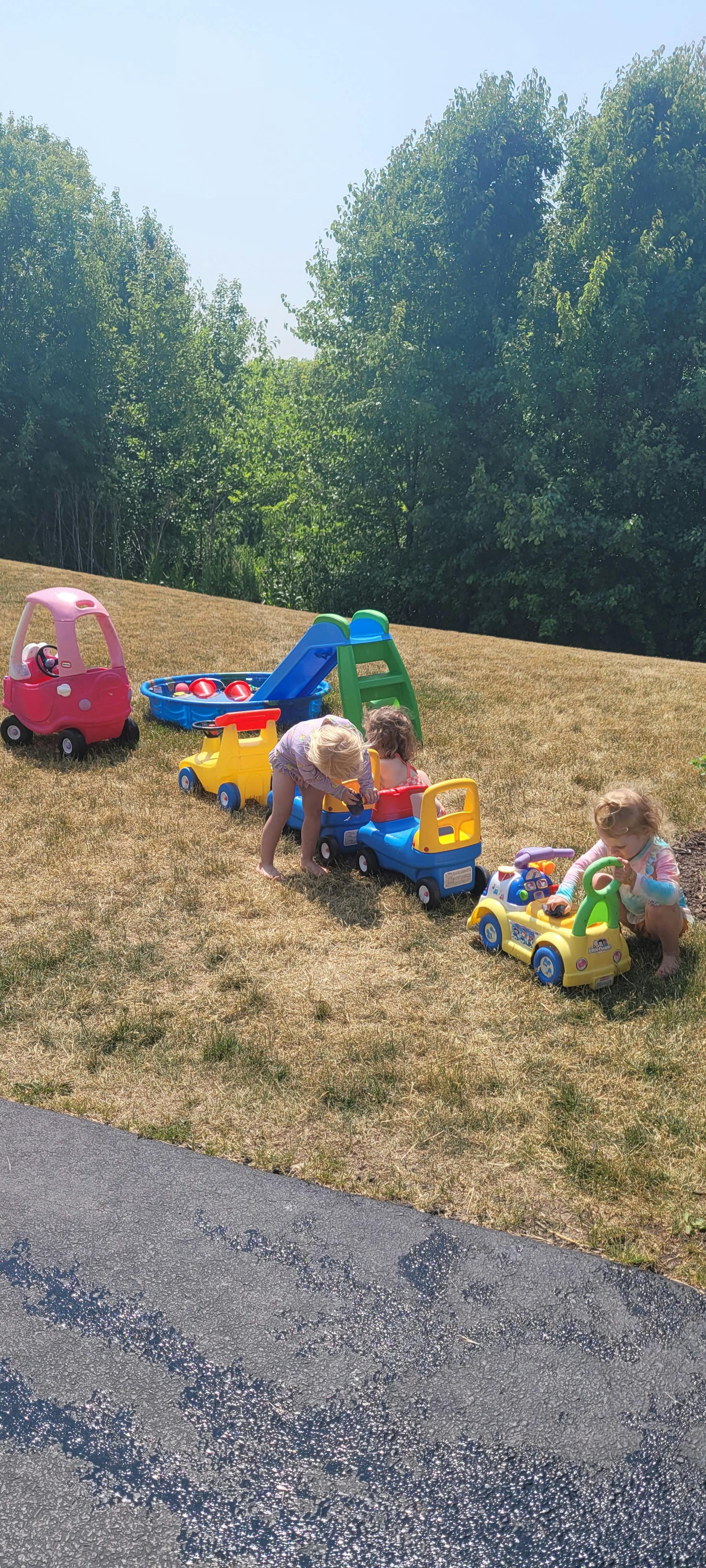 Children playing with toy cars and a slide on a grassy hill