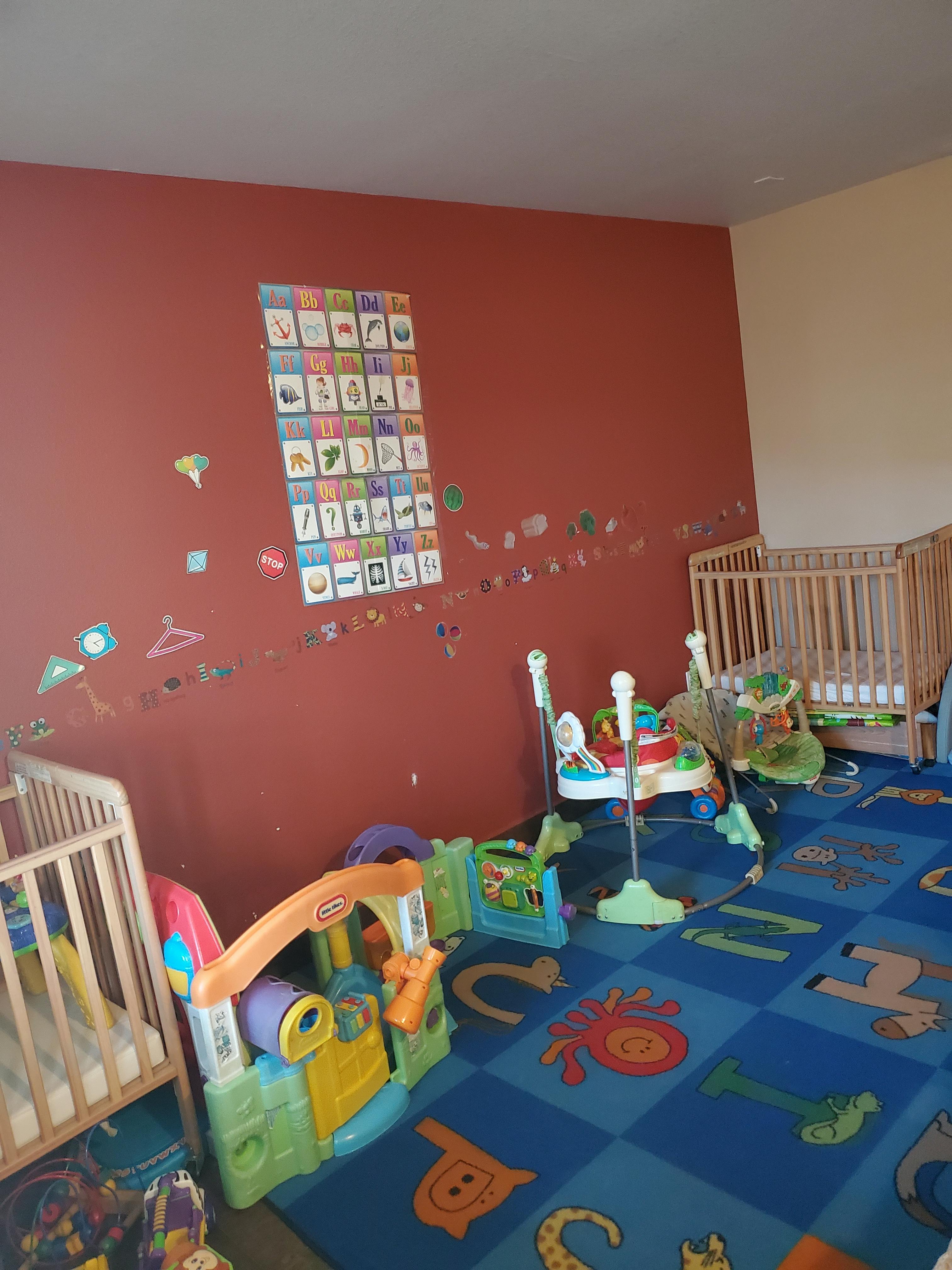 Nursery room with two cribs, play mat, and various baby toys