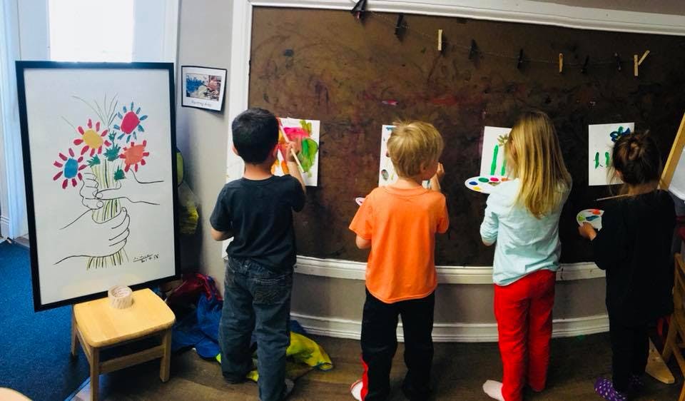 Children painting on paper attached to a wall