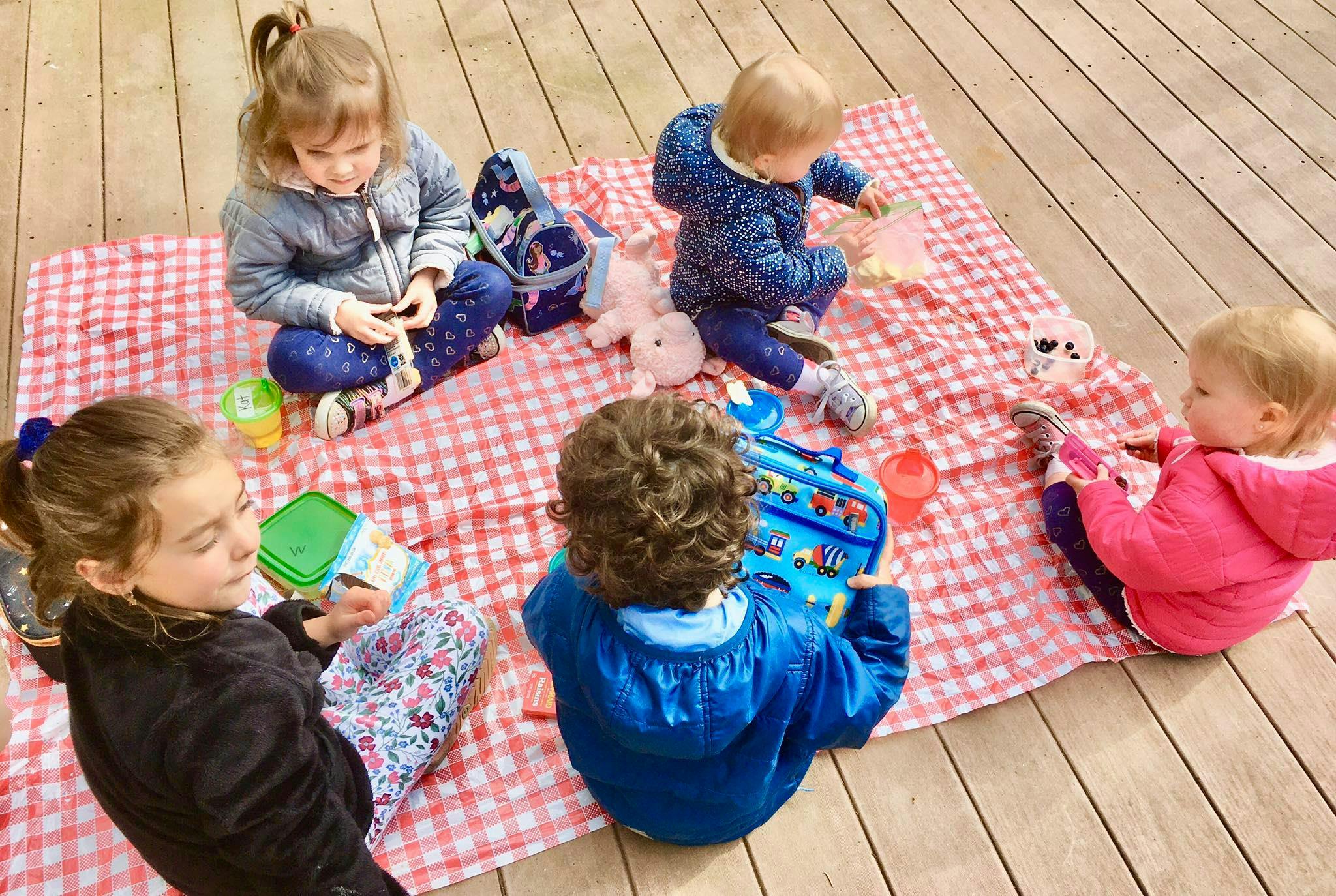 Five children sitting on a red and white checkered blanket